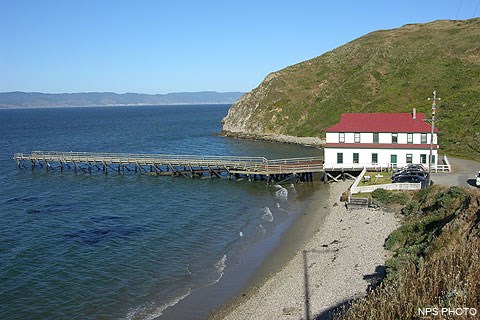 A two-story structure with white walls and a red roof and a dock stretching out into water.