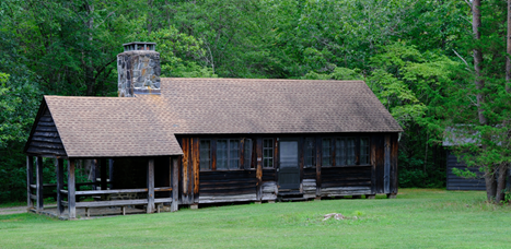 Wooden cabin building with a stone porch and chimney sits next to a dense green forest