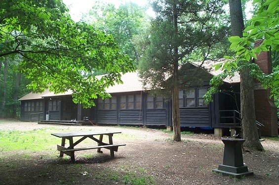 Large wooden cabin with windows, a small porch, and brick chimney at the edge of the forest