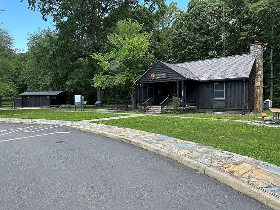 Paved drop off with slope to a stone paved sidewalk leading to a wooden cabin building at the edge of the forest