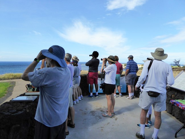 Group of visitors with binoculars looking toward the ocean
