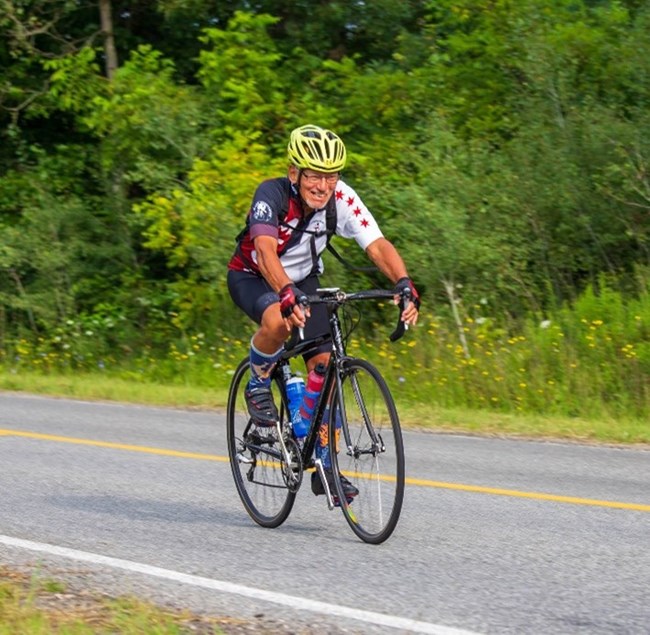 A man rides a bicycle on a trail wearing a green helmet and a Chicago flag themed bike jersey.