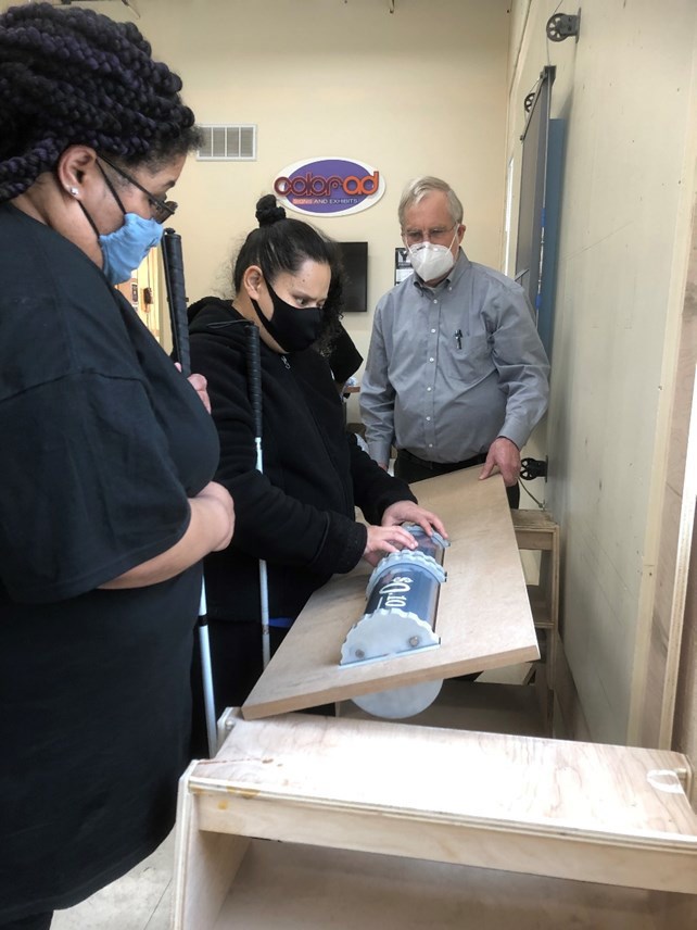 Three people stand around a turn table test exhibit element.