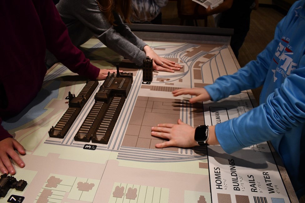 Three visitors explore a tactile bronze and plastic map with their hands