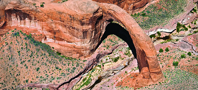 Aerial shot of Rainbow Bridge. a few bushes and rocks underneath.