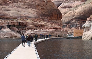 Visitors walk down floating dock in canyon toward floating restroom building