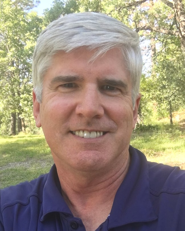 A smiling man with white hair and a blue shirt.