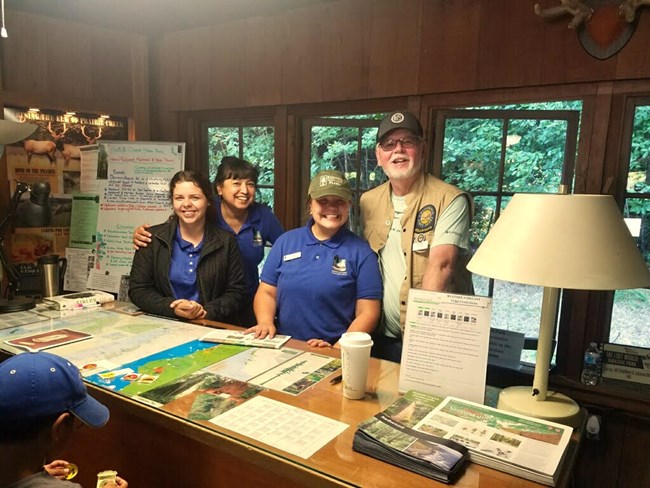 Four smiling staff stand behind a wooden desk at a visitor center.