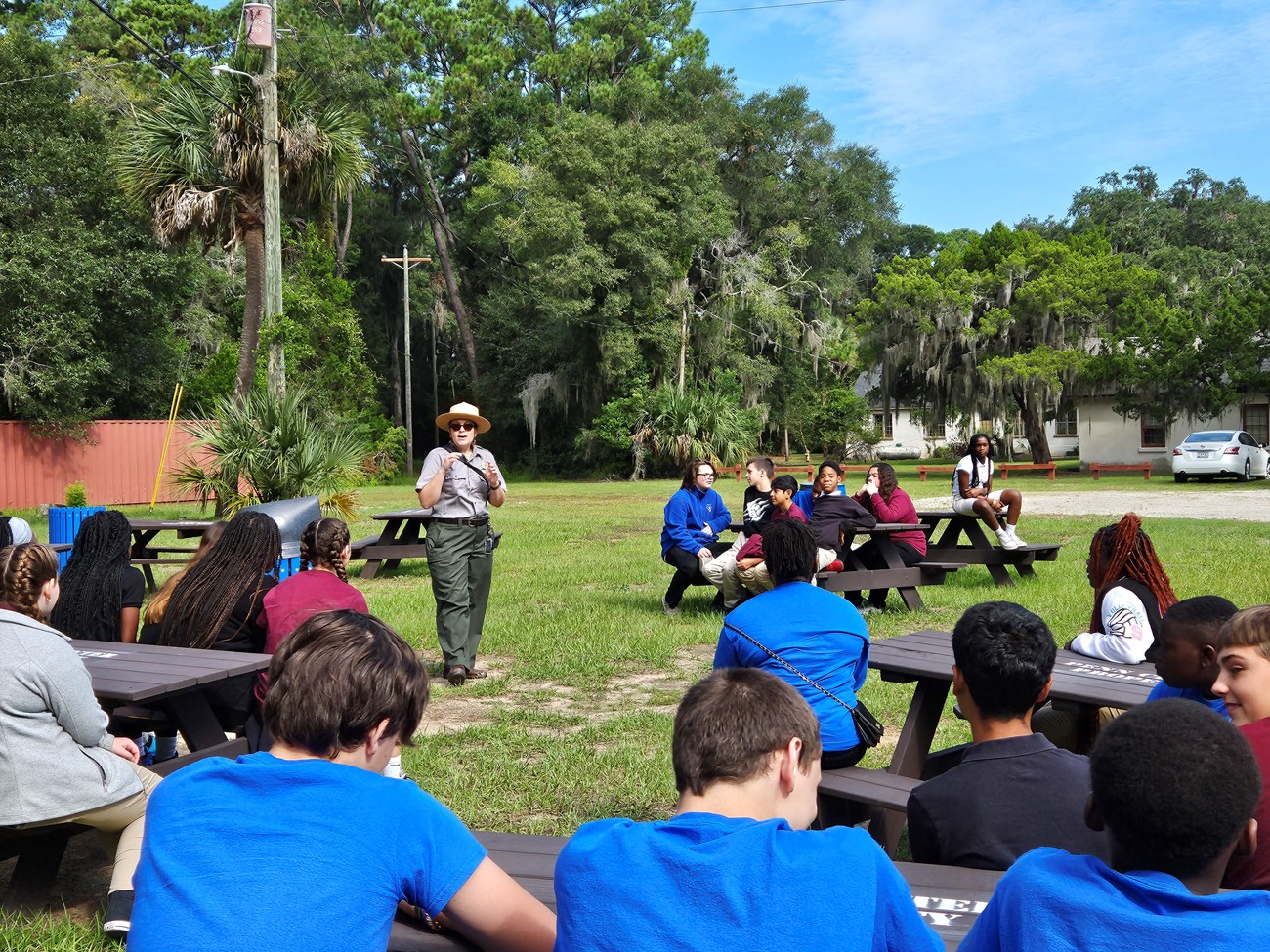 A ranger speaks to a group of teenagers who are sitting at picnic tables