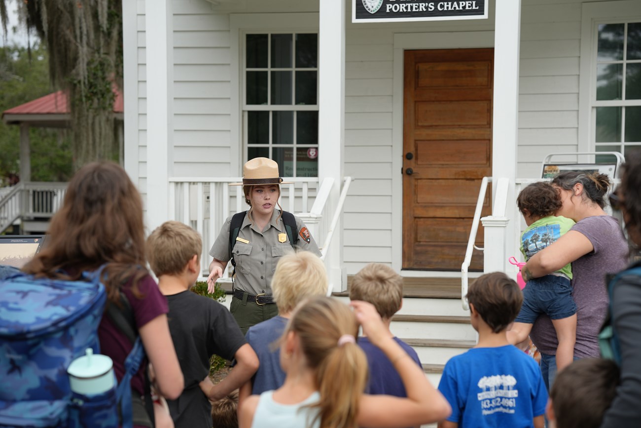 A ranger talks to a group of students in front of a white chapel.