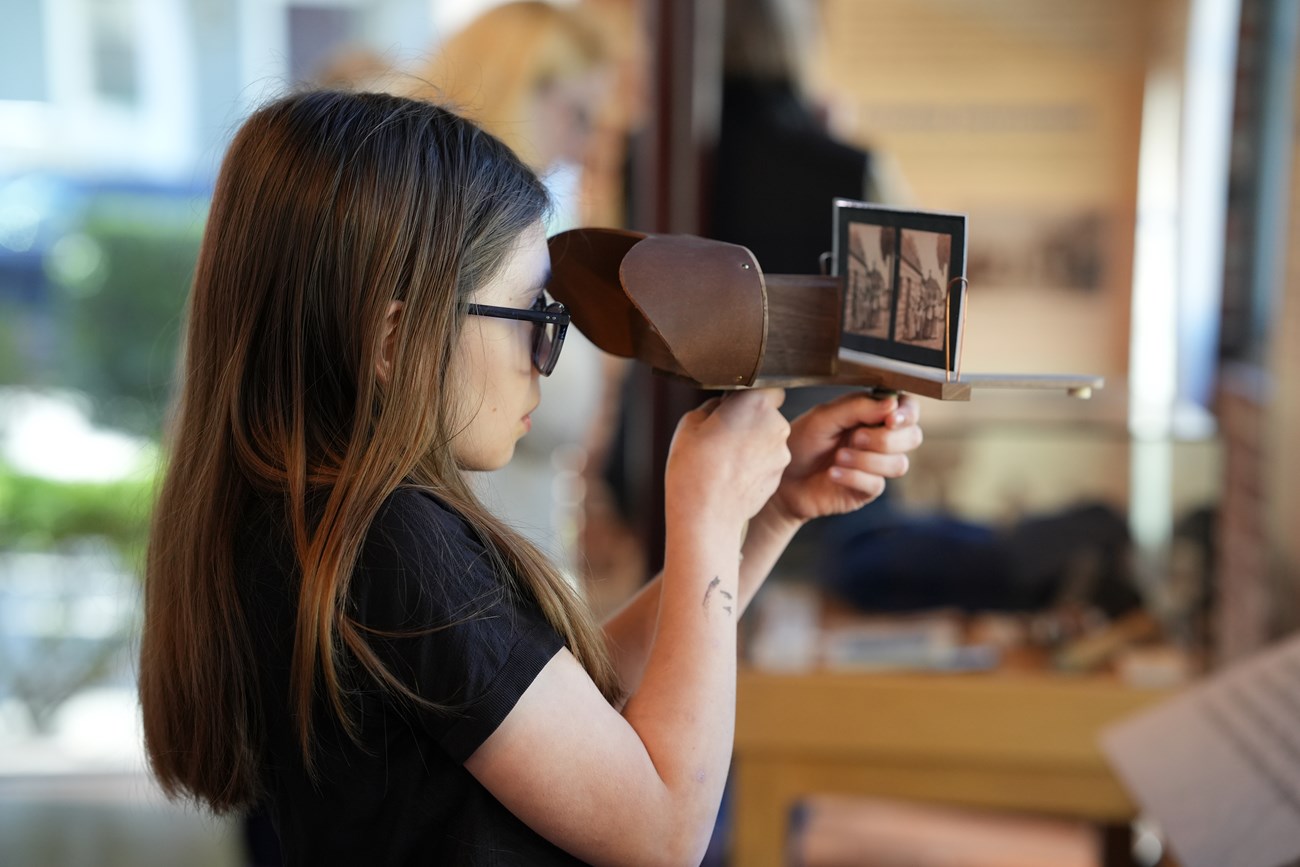 A young girl looks through a wooden stereoscope at an image.