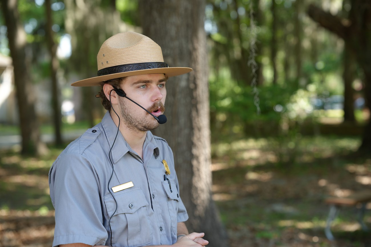 A ranger talks to the public outside wearing a microphone.