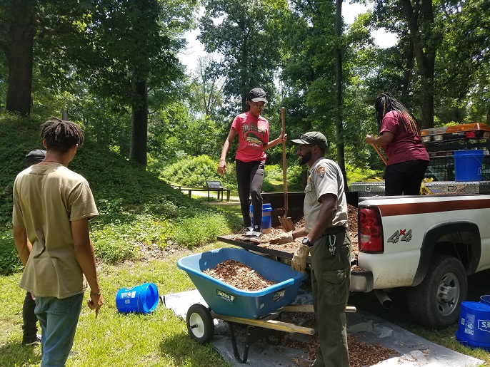 A park ranger with youth workers shoveling earth from the bed of a pickup truck.