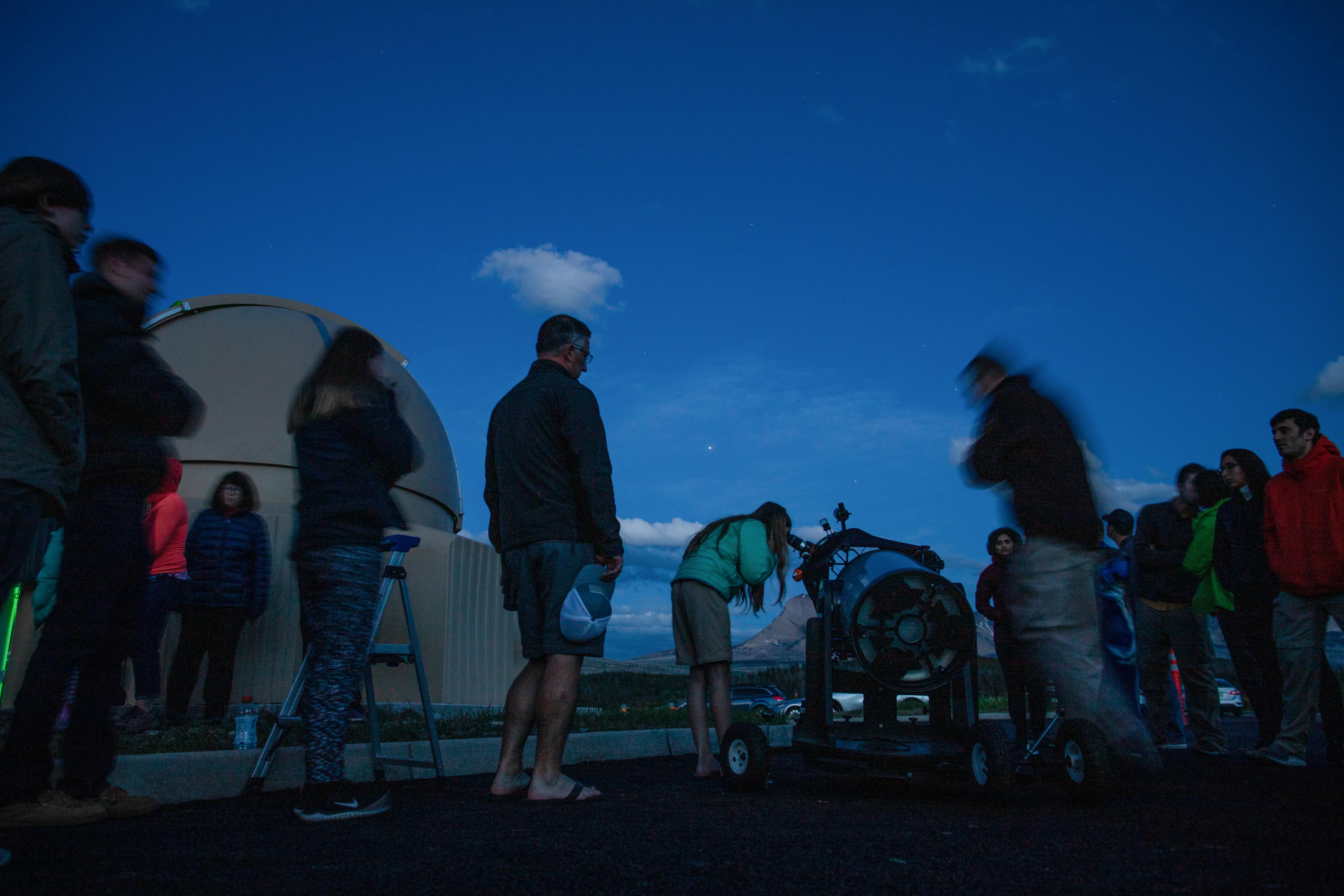 A group of people look through telescopes at twilight