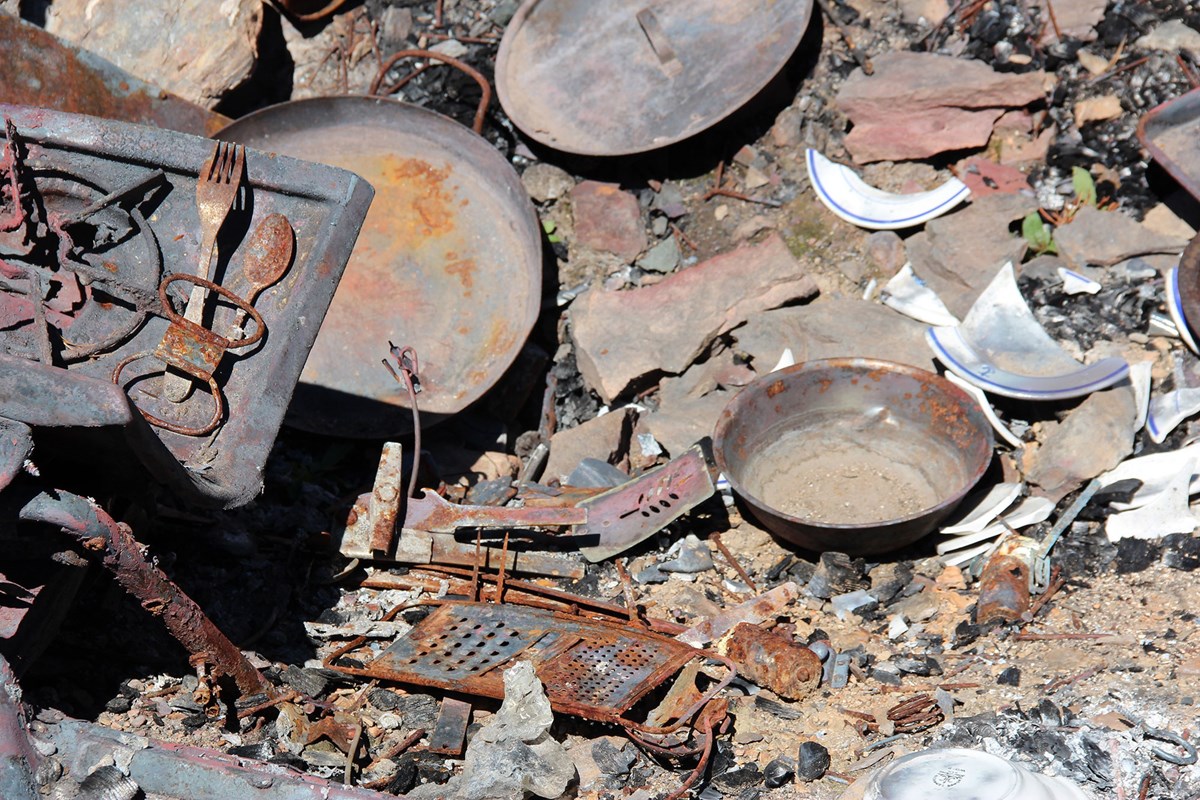 Rusted, old pans and utensils, broken plates, and a rusted, metal cheese grater lie in a pile.