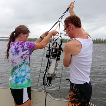 Two students remove water quality testing equipment from the water.