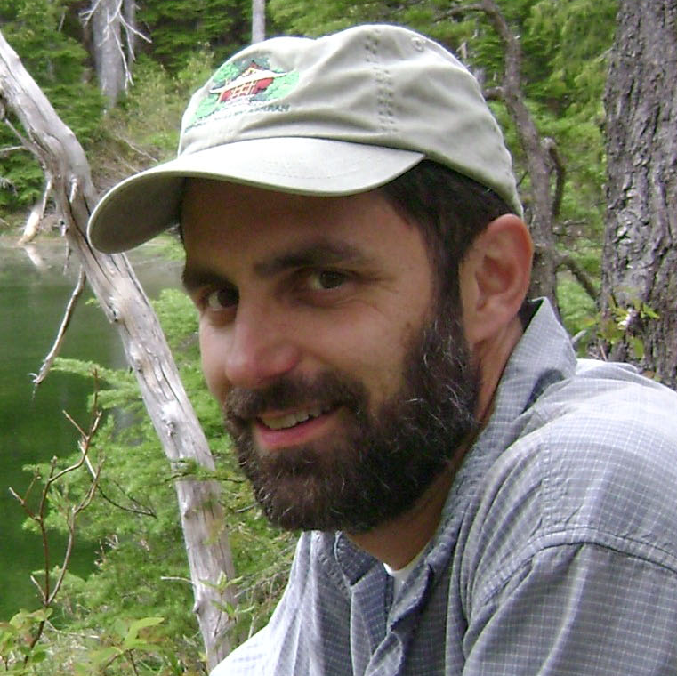 Headshot of John Boetsch, a smiling white man outdoors with a dark beard and a ball cap.