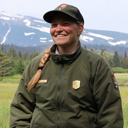 Image of a person in a green uniform with a meadow and mountains in the background.