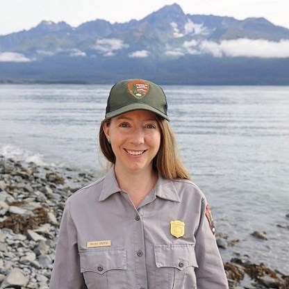 Image of a person in a grey shirt with ocean and mountains in the background.