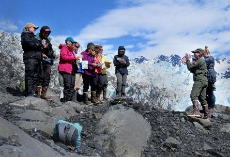 Teachers stand on a hillside overlooking a glacier.