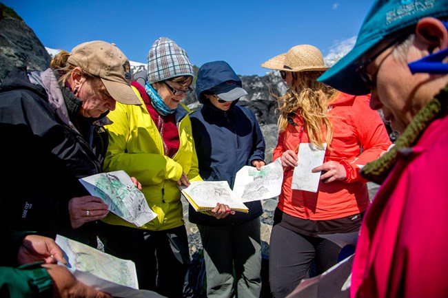 A group of people stands in a circle holding drawings of mountains.