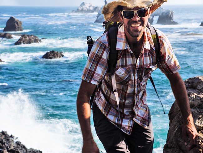 Keith smiling as he hikes along a rocky section of coastline