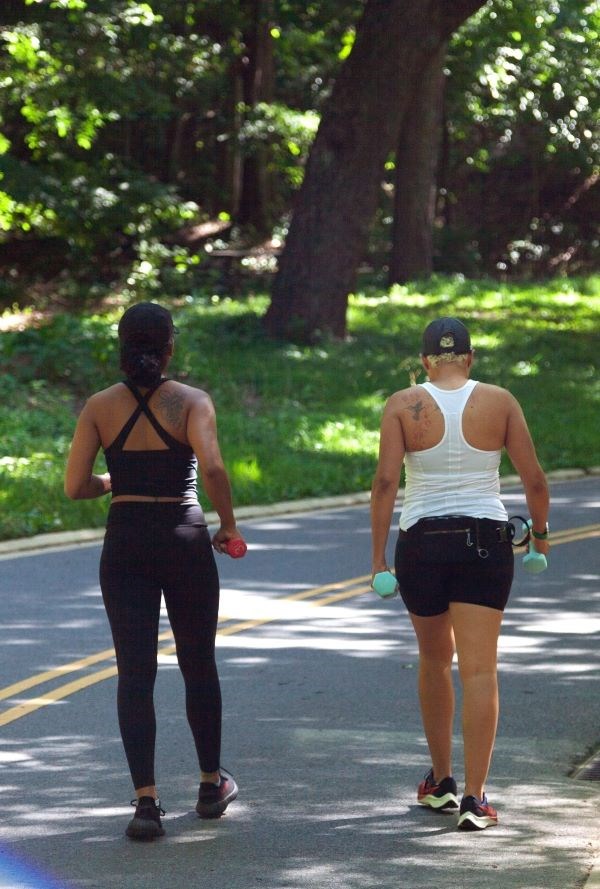 Two visitors walk down a park road holding weights.