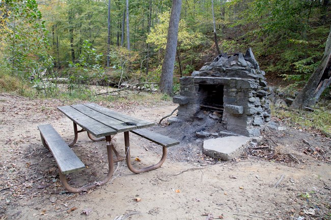 A picnic table sits beside a stone chimney grill.