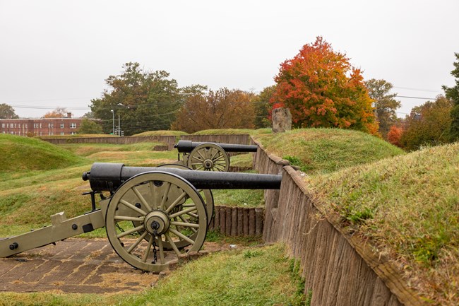 A pair of civil war era cannons are positioned on a hillside with autumn trees in the background.