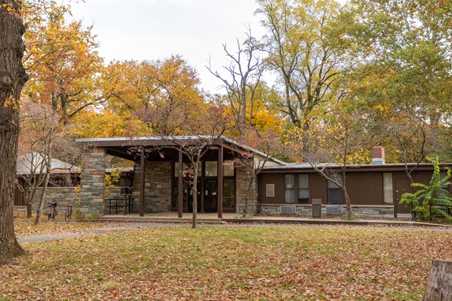 A wide, brown one story building surrounded by trees with fall colored leaves.