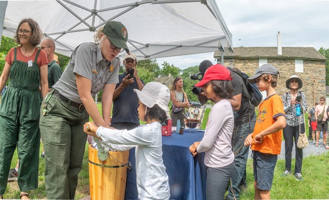 Park ranger helps a young girl crank an ice cream churn