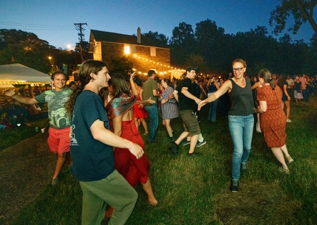 Dozens of people square dance at dusk