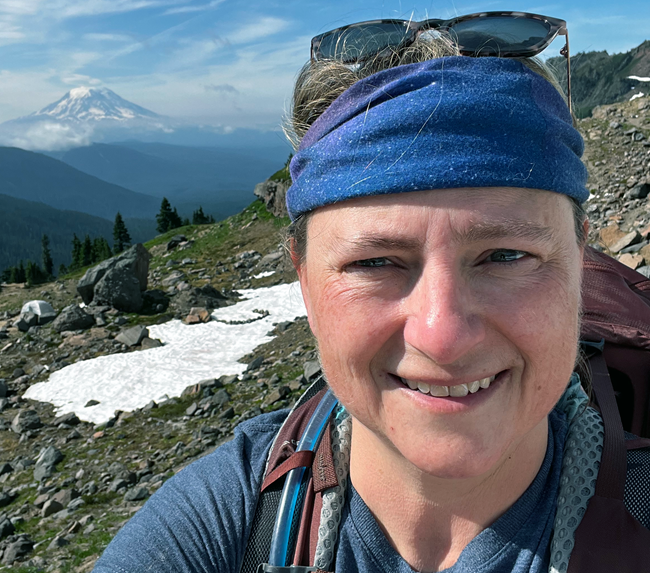 Headshot of Jennifer Ball, outside while hiking with a mountain in the background