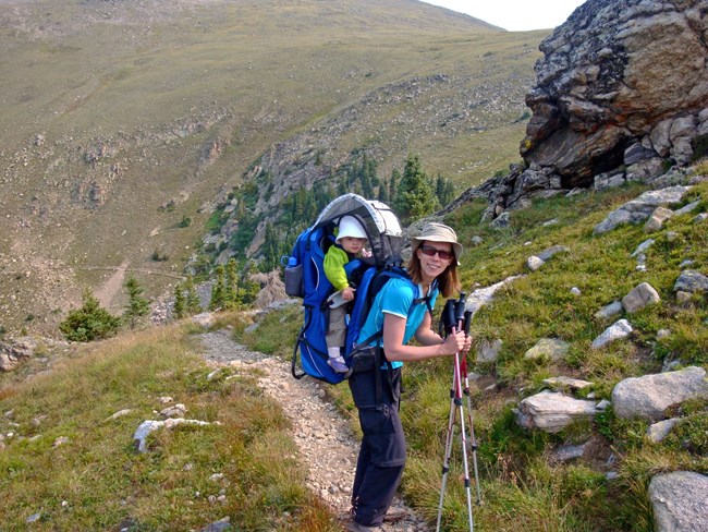 A hiker is carrying a baby inside a backpack while on the Tonahutu Trail in summer