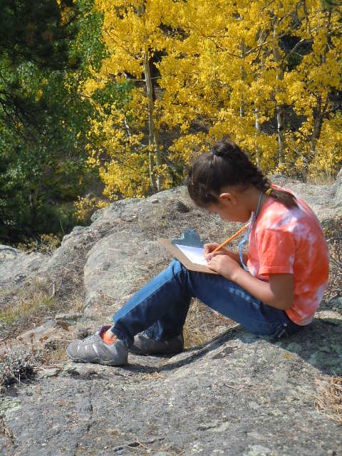 young student sitting on a rock and writing