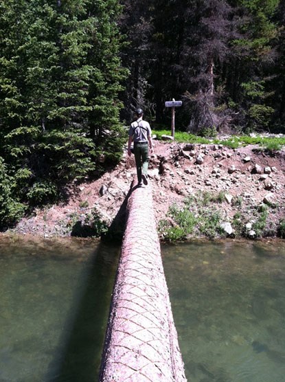 Backcountry Ranger hiking over a footbridge in Rocky Mountain National Park.