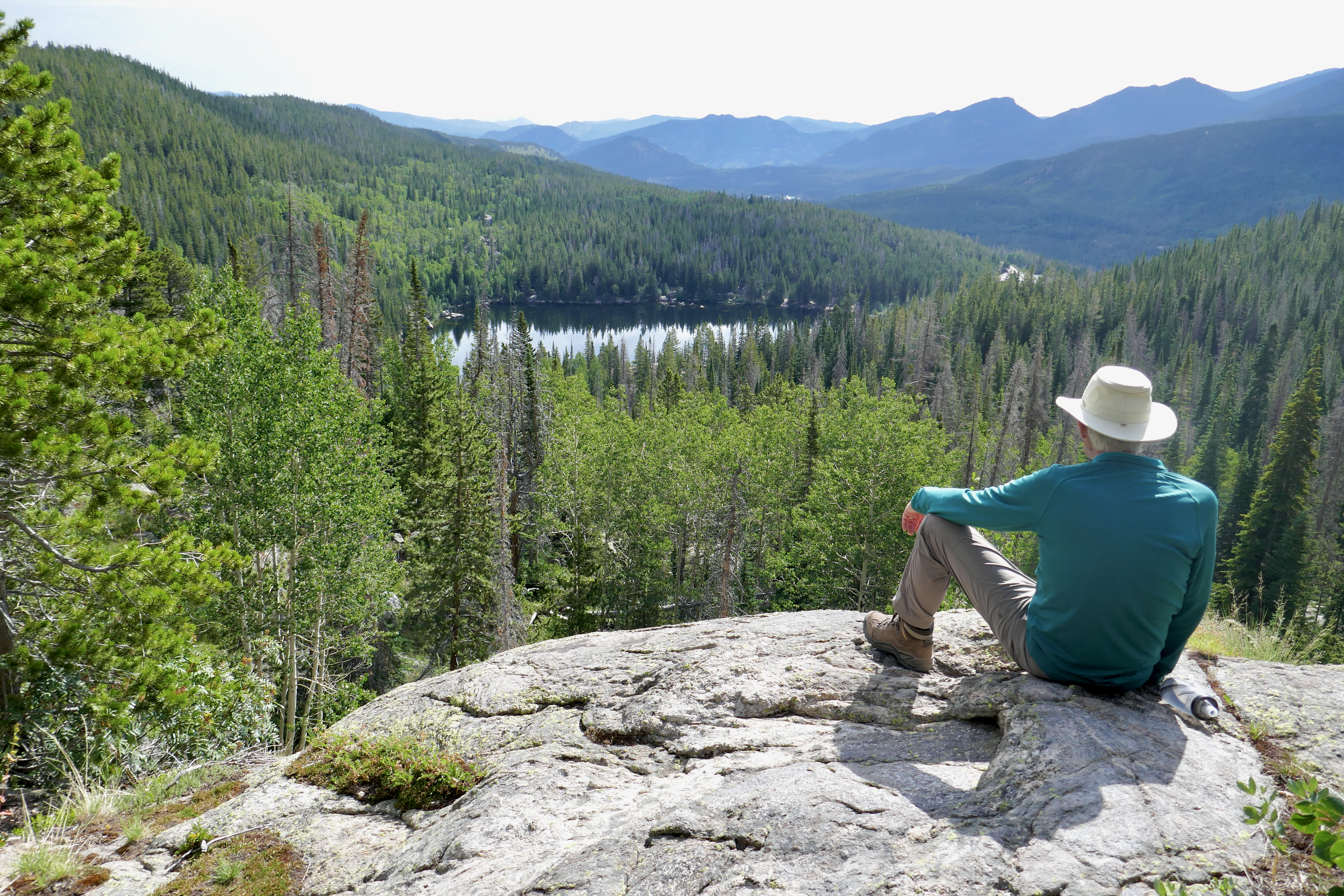 A hiker is sitting on a rock and enjoying a scenic view in the distance