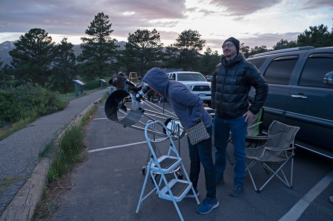 A park visitor is looking up at the sky using a telescope in June
