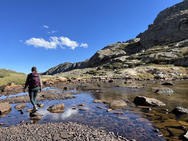 A hiker is walking on rocks across a path with water in spring