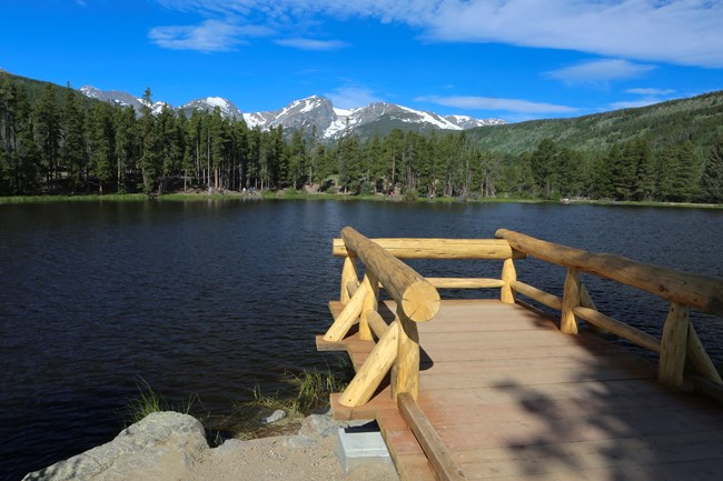 A wooden dock on a lake shore with mountains in the distance.