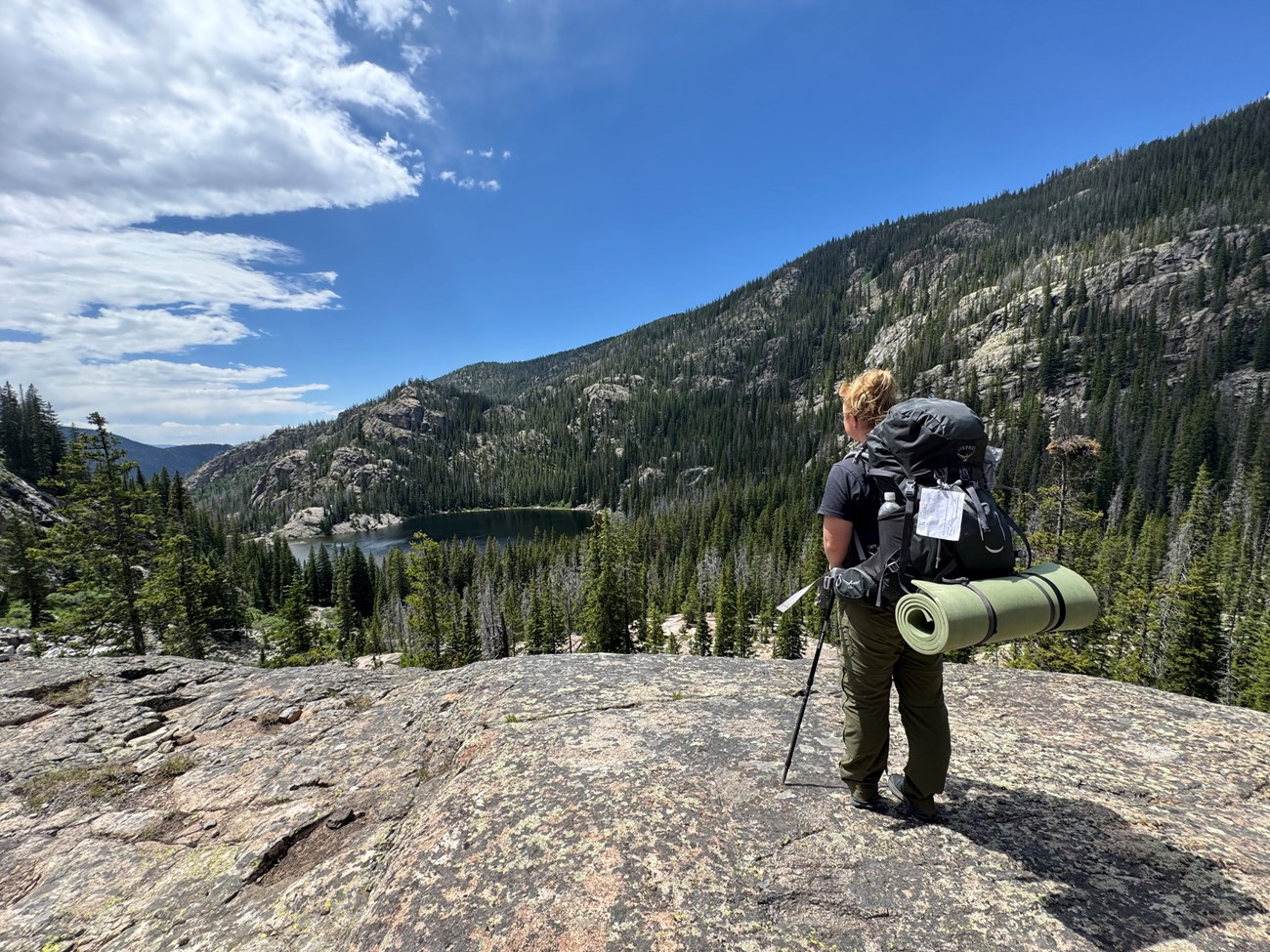 A person carrying a wilderness backpack full of gear is gazing out at a lake