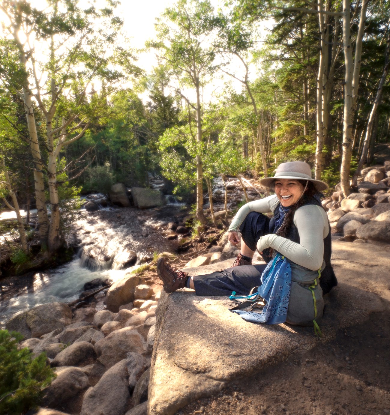 A park visitor is sitting down near Alberta Falls and smiling when looking towards the camera