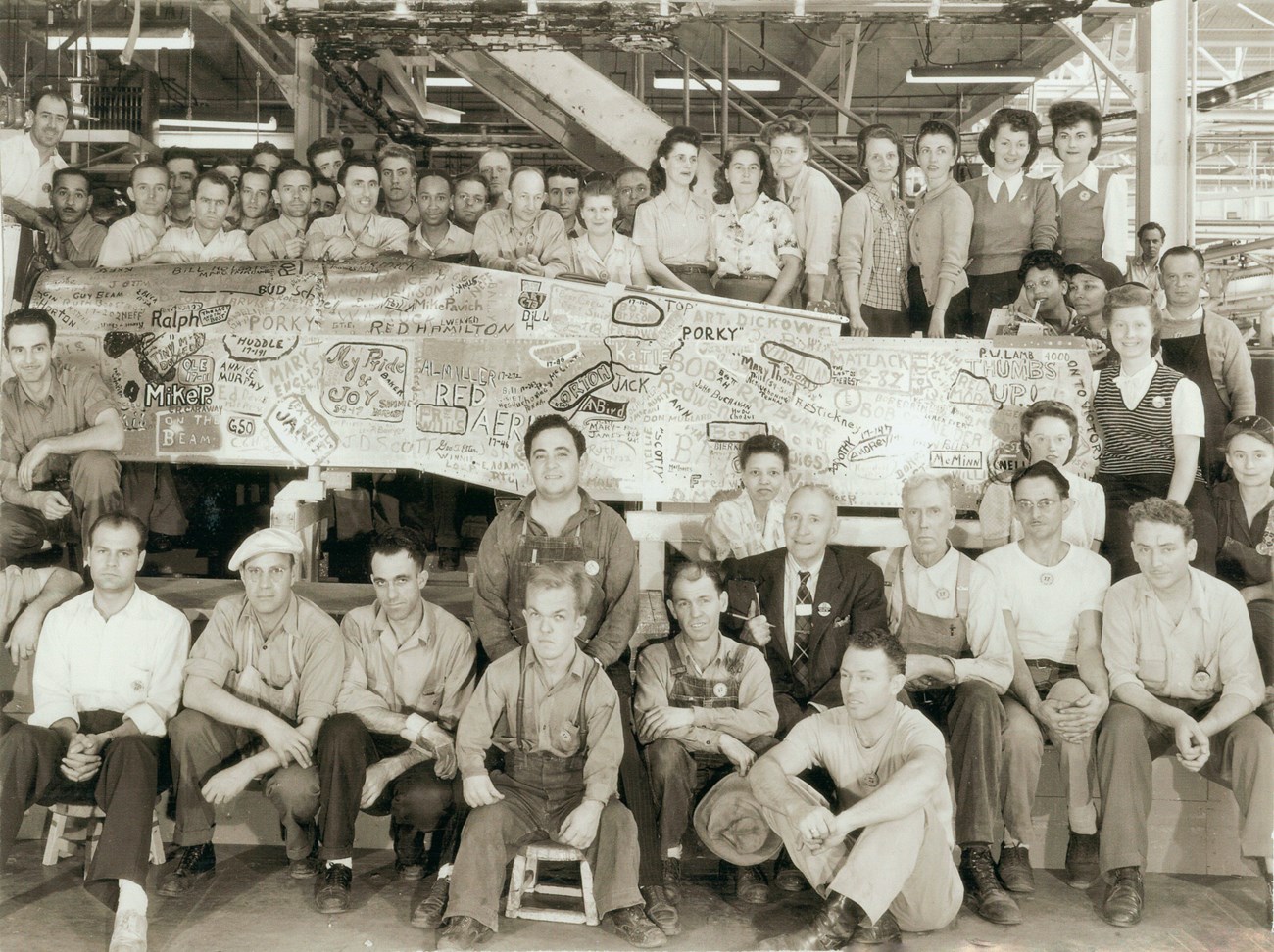 A crew of home front workers pose for the camera. A banner signed by many is held up.