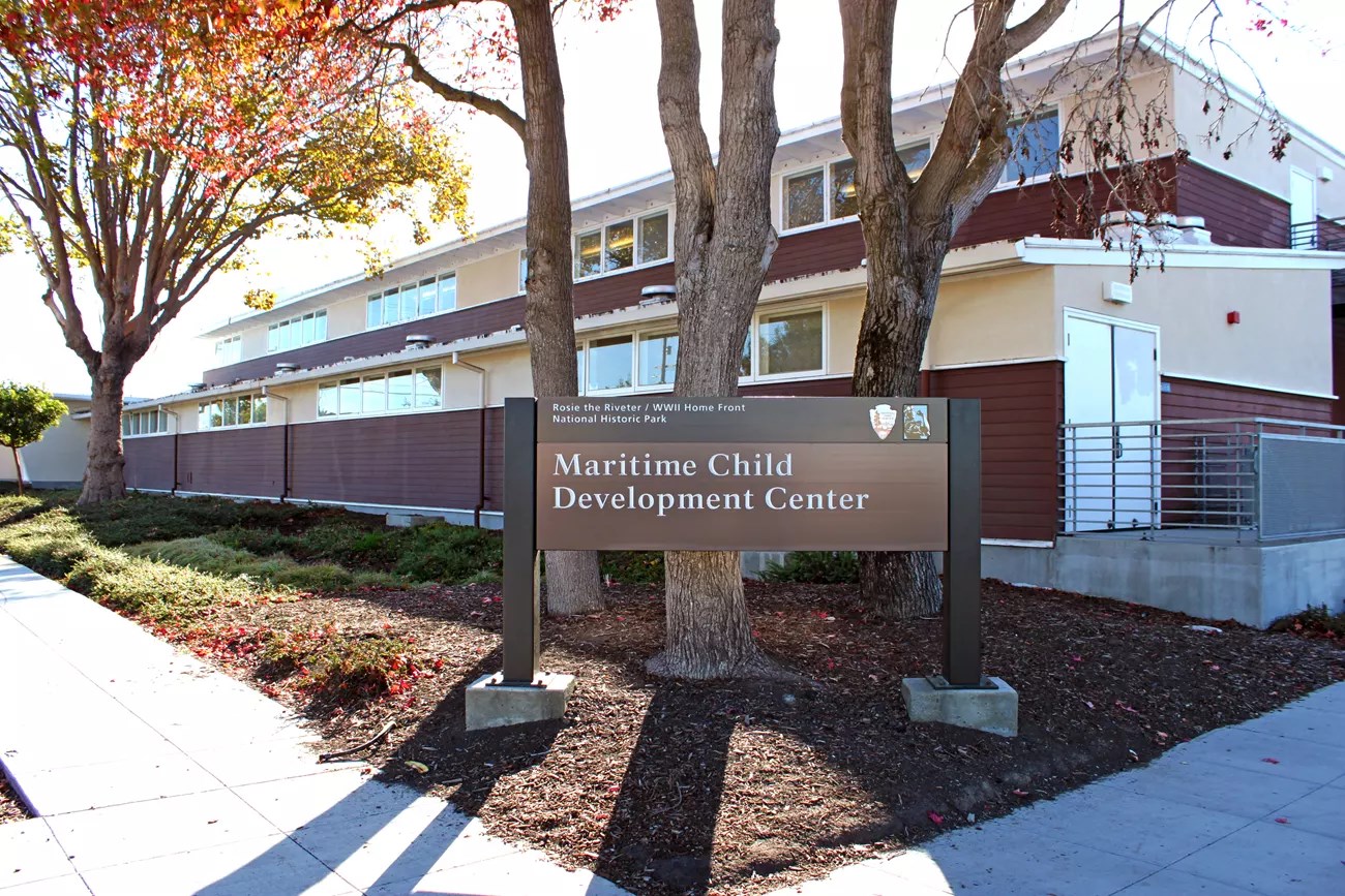 Sign for the Maritime Child Development Center in front of a building surrounded by trees and landscaping.