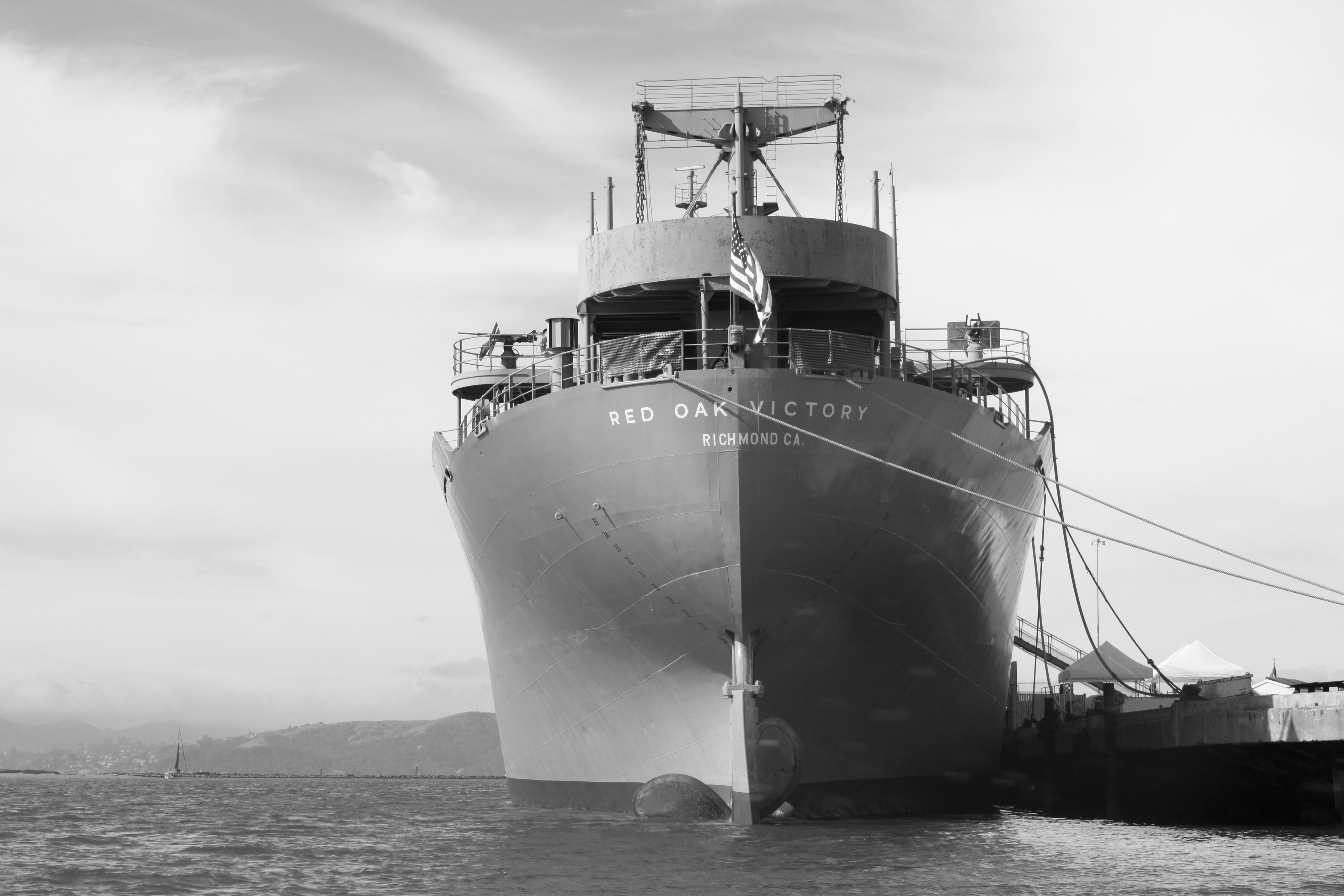Black and white photo of the SS Red Oak Victory ship docked at a pier in Richmond, California, with its name prominently displayed on the hull and an American flag flying at the stern.