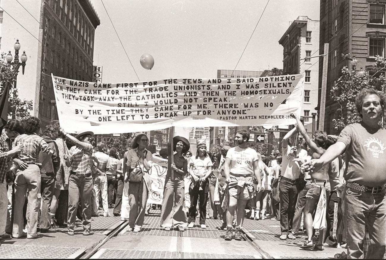 Historic photo of people marching in parade, holding a banner.
