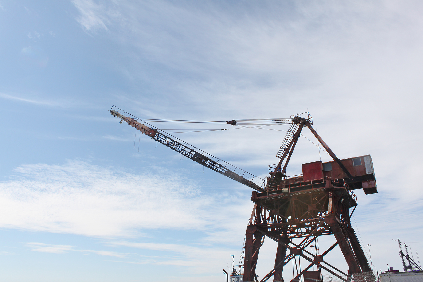 A large, rust-colored Whirley Crane with an extended boom stretches into a partly cloudy sky. The intricate lattice structure of the crane is visible, showcasing its robust industrial design.