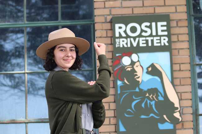 Young female ranger doing the Rosie pose in front of park sign.
