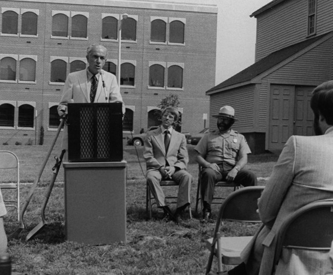 A man at a podium giving a speech in a grassy areas