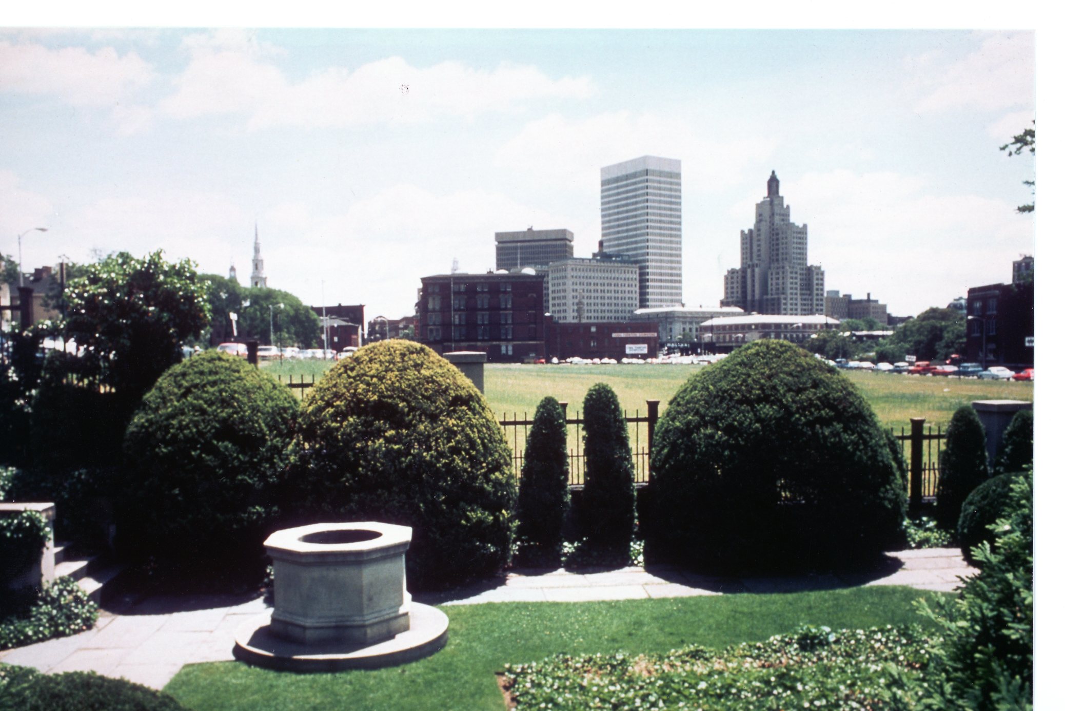 color photo of the stone well, park grounds, and downtown sklyine